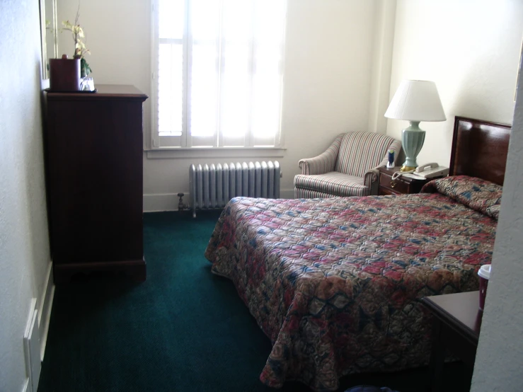 a small el room features a bed, chairs, dresser and window