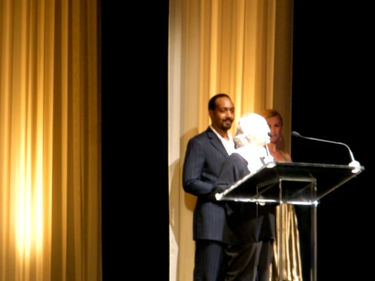 a man speaking into microphone in front of curtains