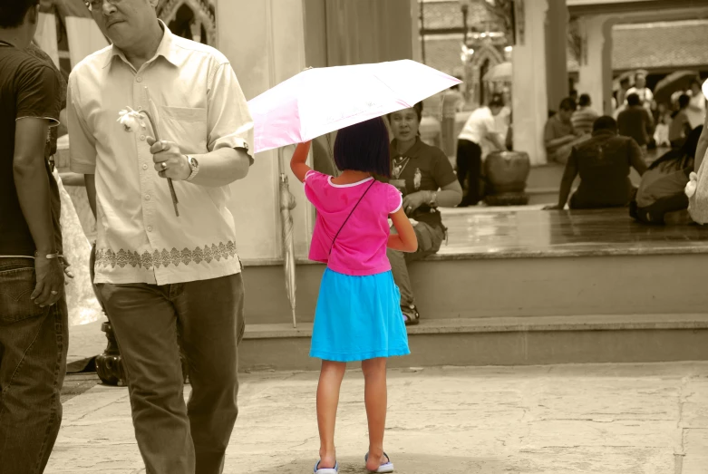 a little girl holding an umbrella as someone walks by