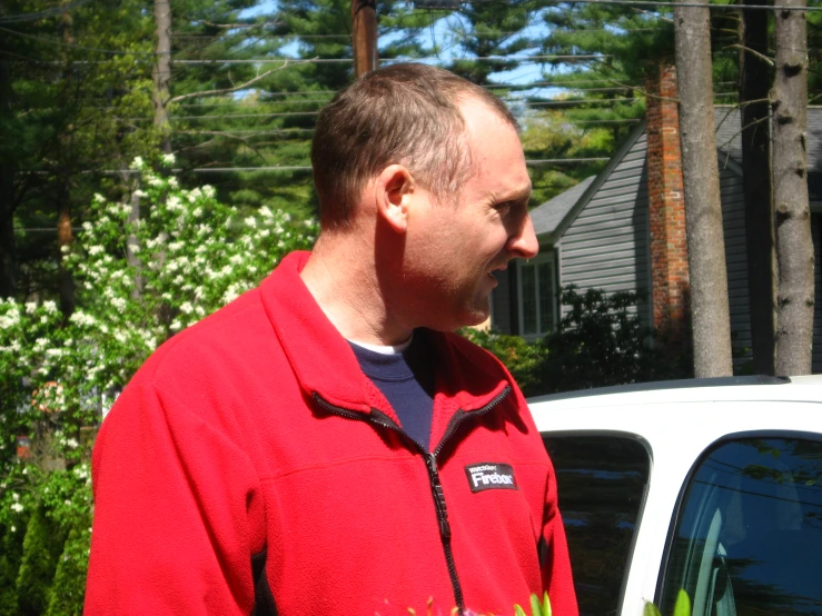 man in red jacket standing in front of white car