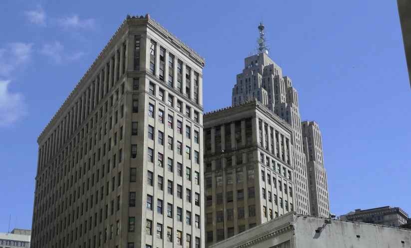 two tall buildings are in a city with blue skies