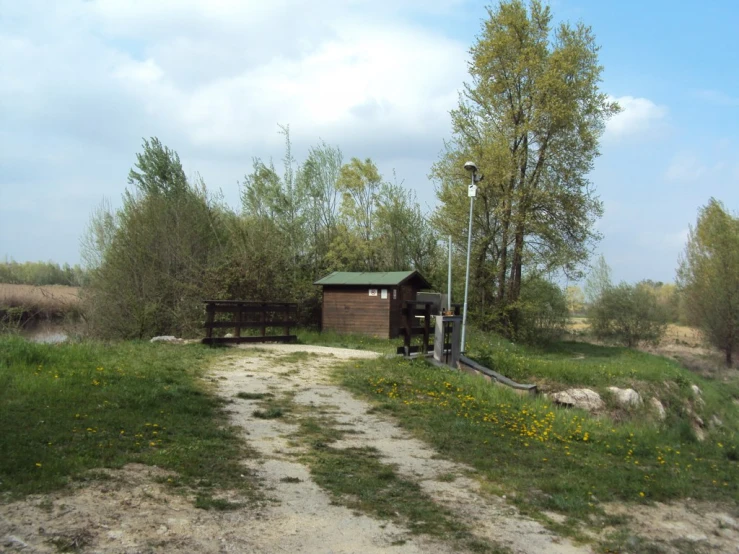 a green roofed, dirt path with green benches and a light post