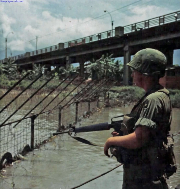 military soldier holding a machine gun standing near water