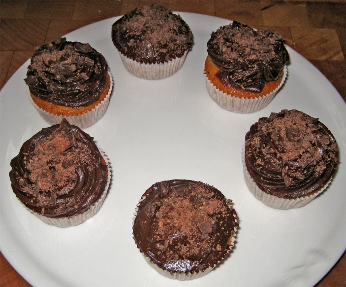 four cupcakes sit on a white plate with one cut in half and decorated with chocolate frosting