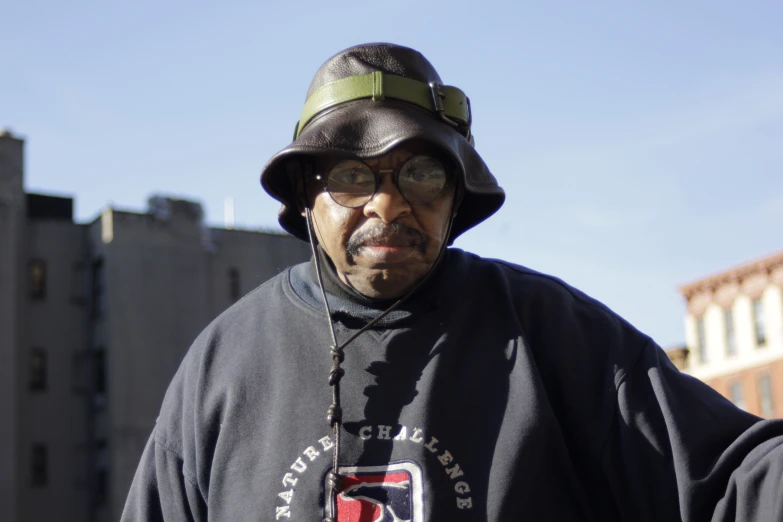 an older man wearing a black hat and glasses is standing with a building in the background