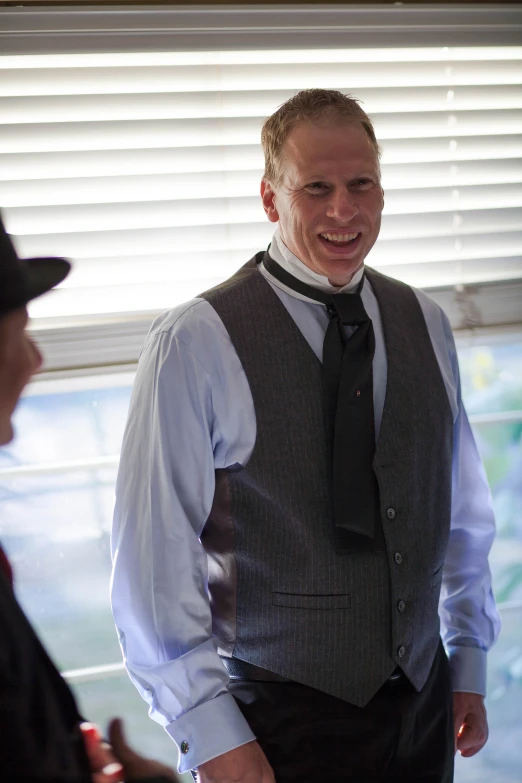 a man wearing a vest smiling and talking to another man