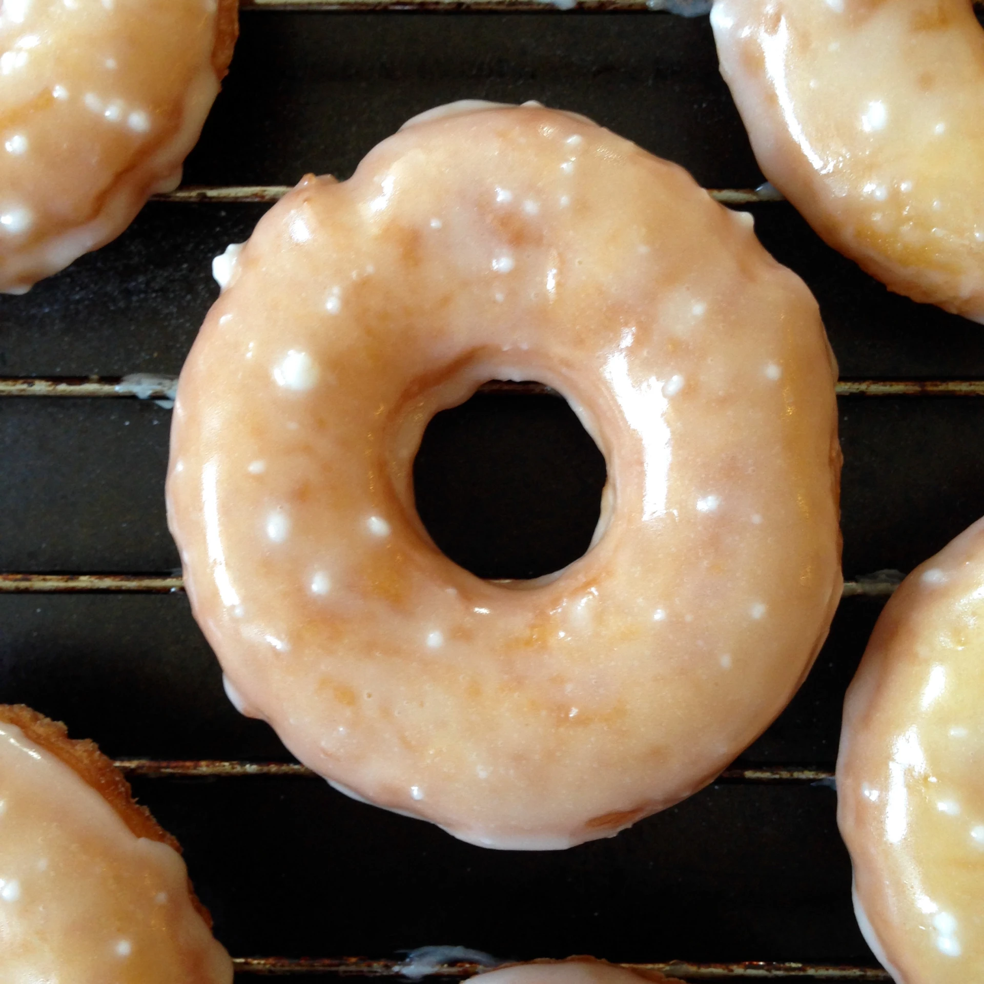 a close up of many glazed doughnuts on a rack