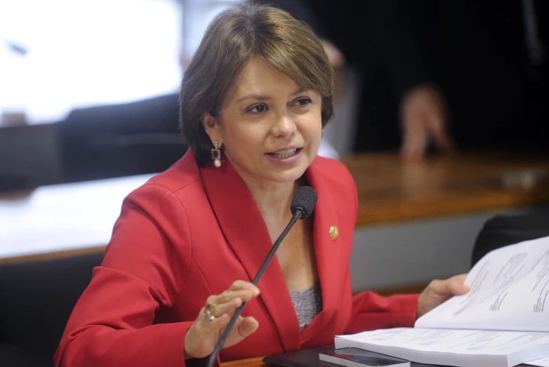 a women in a red suit talking on a microphone at a table