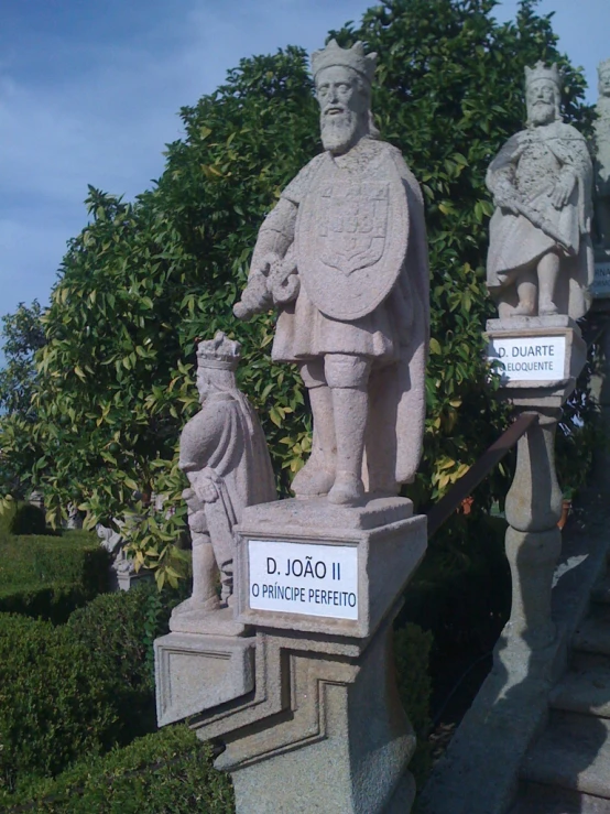 statues of a man and two woman in formal clothing with trees in the background