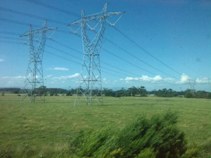 two power poles in an open field with a grassy land behind them