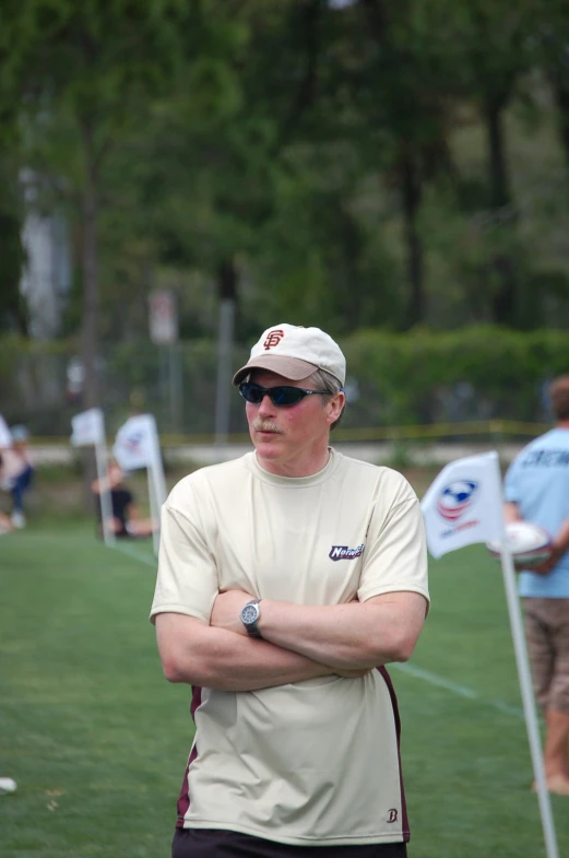 a man in a hat and sunglasses is standing with his arms crossed