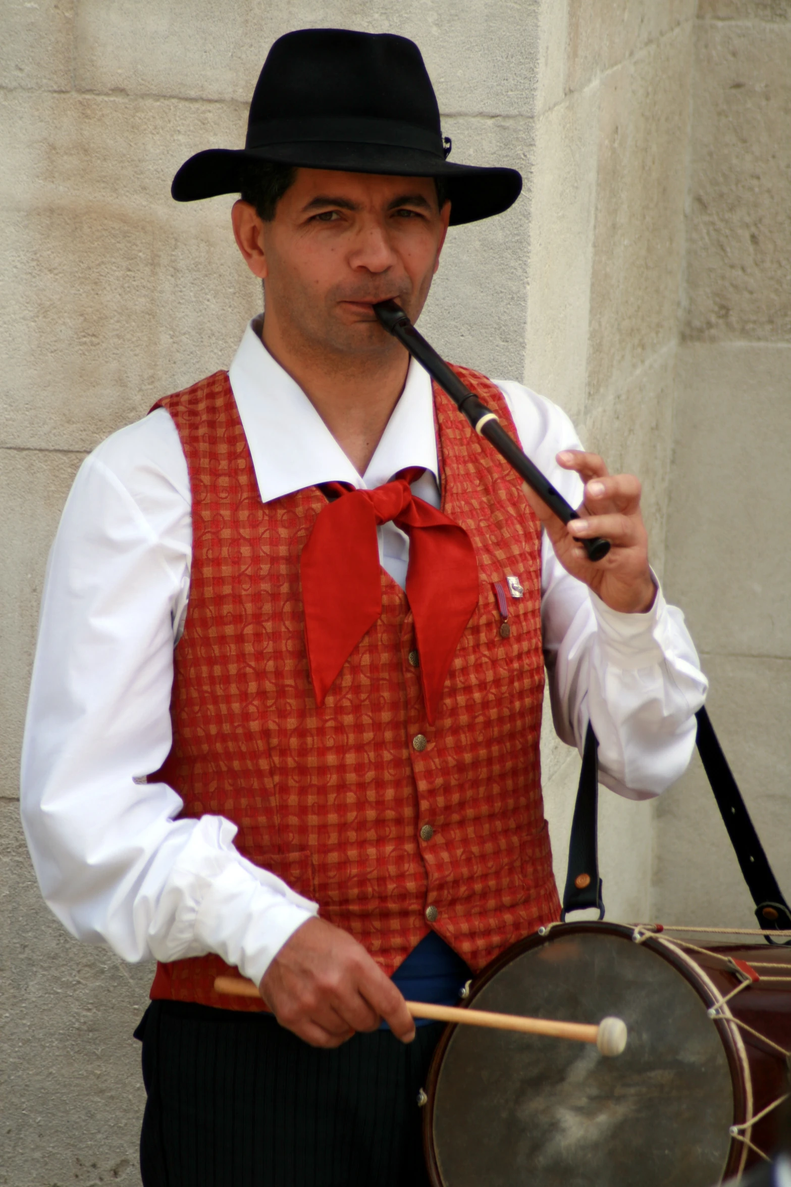 the man is wearing an orange vest and black hat playing the drum