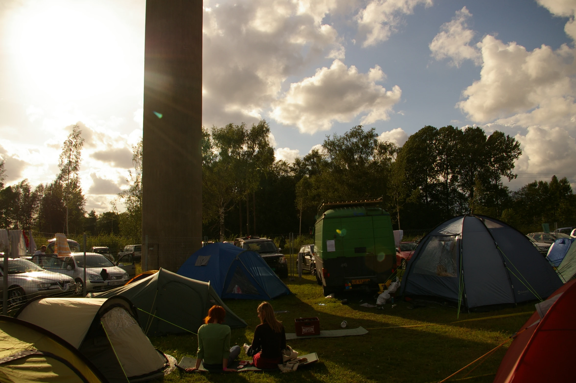 three women are sitting on the grass near tents and trees