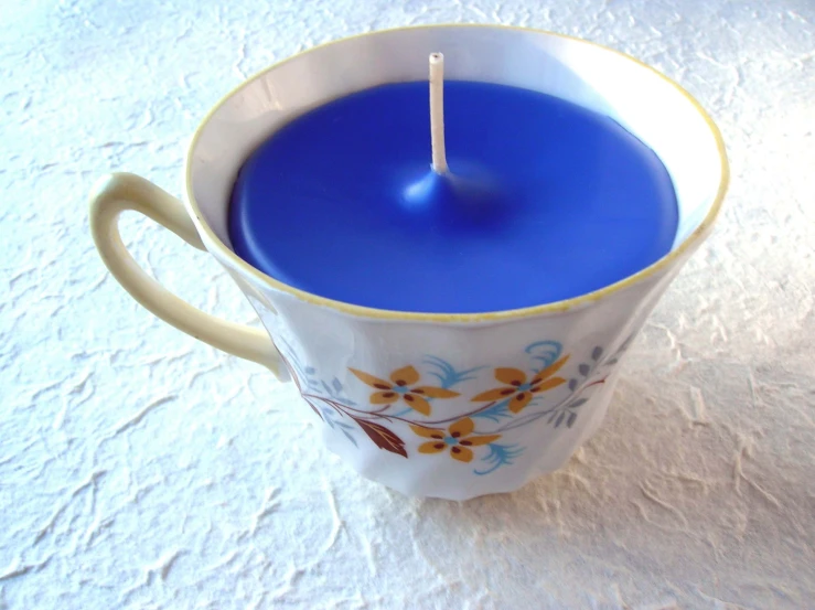 the candle is inside of a mug on a white cloth