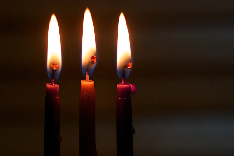 three lit candles in a dark room with the light turned off