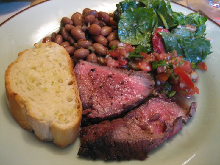 meat, beans and greens sit on a plate with bread