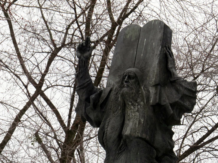 the statue of the devil is posed in front of bare trees