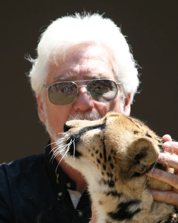 an older man with sunglasses is giving a large cheetah soing