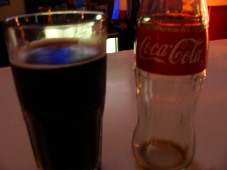 a bottle of cola and a tall glass of coke sitting on a table