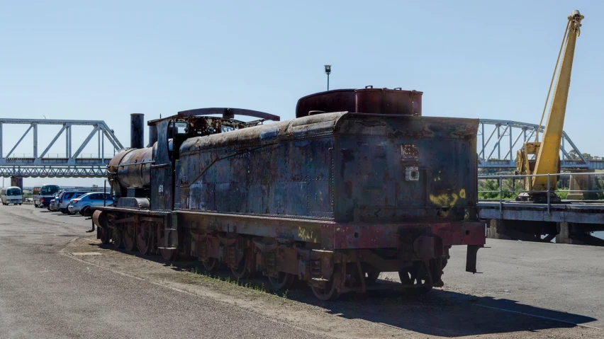 a rusted out, rusty train in front of a bridge