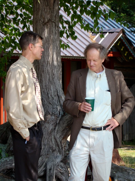 two older men in business attire stand near a tree