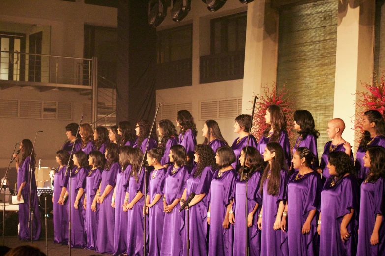 a group of women in long purple dresses standing on stage with microphone