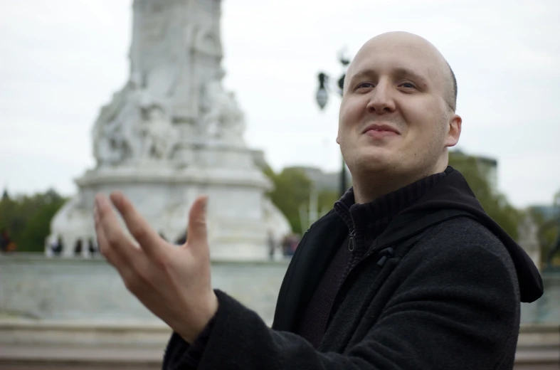 a bald man standing in front of a monument holding his hands out