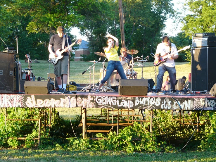 a band on stage with guitar players at outdoor event