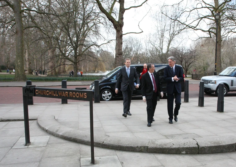 three men walking in a circle near cars