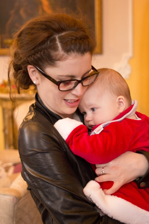 a woman in black jacket and glasses holds a baby