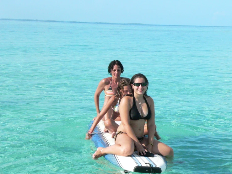 three girls riding on a boogie board in the ocean