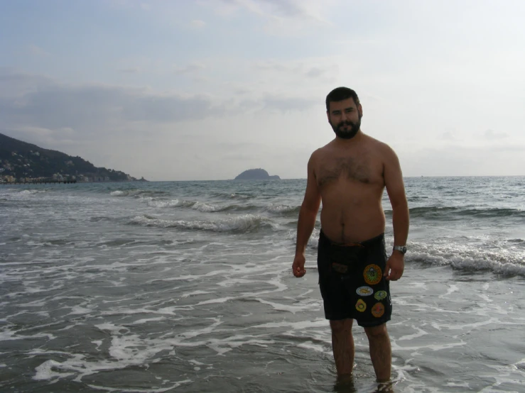 a bearded man standing in the ocean holding a snowboard