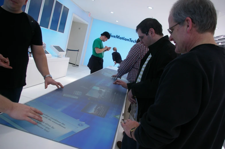 men are standing around looking at a display in the center of a room