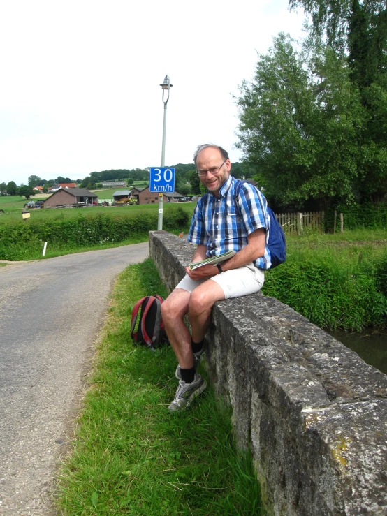 a man wearing white shorts and a blue checked shirt sits on a stone bench