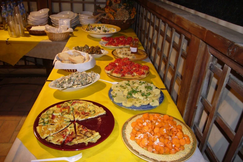 an array of food on yellow table cloths on a dining room table