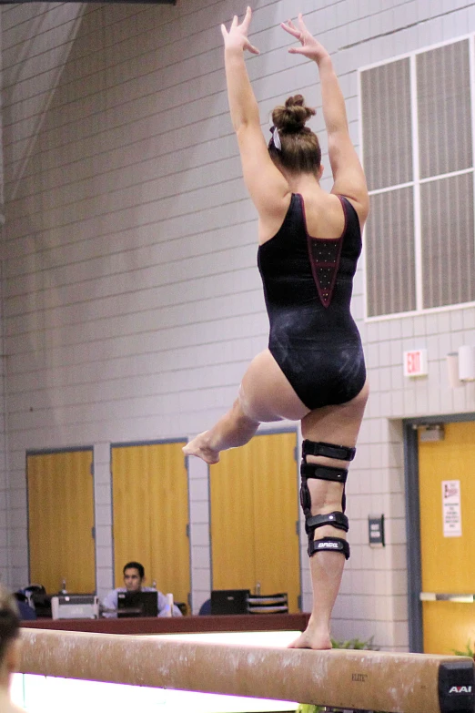 a female in a black gymnastics outfit doing a flip on a balance beam