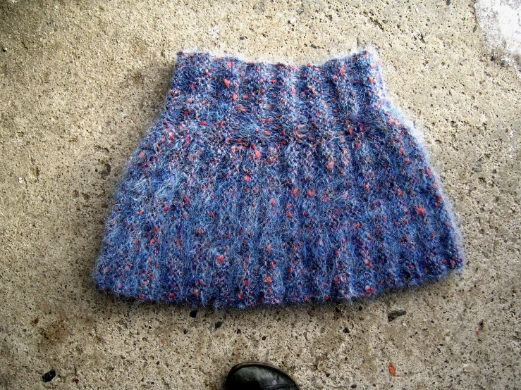 a blue knitted hat sits on the ground next to a shoe