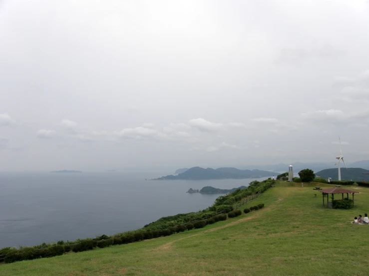 people are sitting and lying on a grassy hill overlooking the water