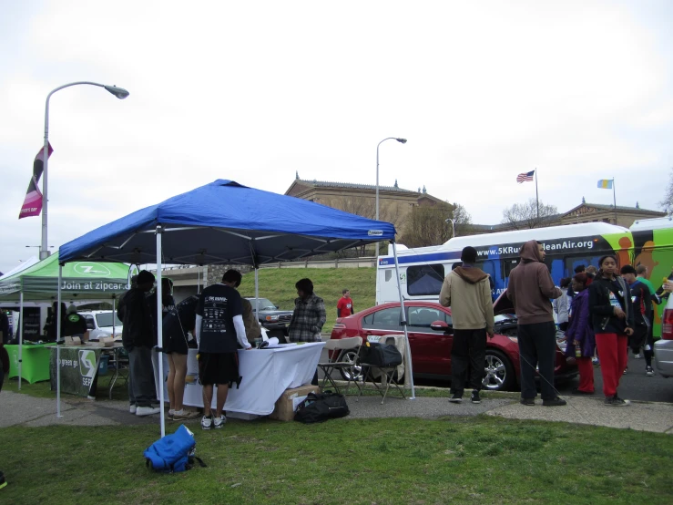 people standing around and eating under a large blue tent