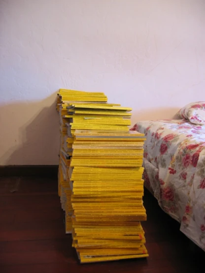 stack of yellow books on the floor near a bed