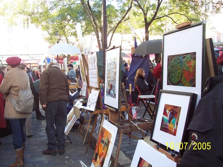 a couple of people walking down a sidewalk past many paintings on easels