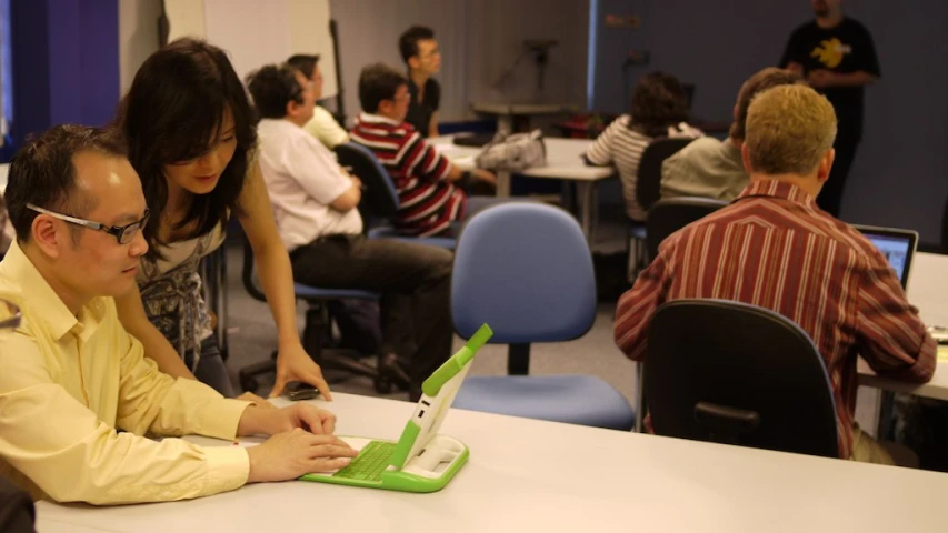 several people in a large room working on a laptop