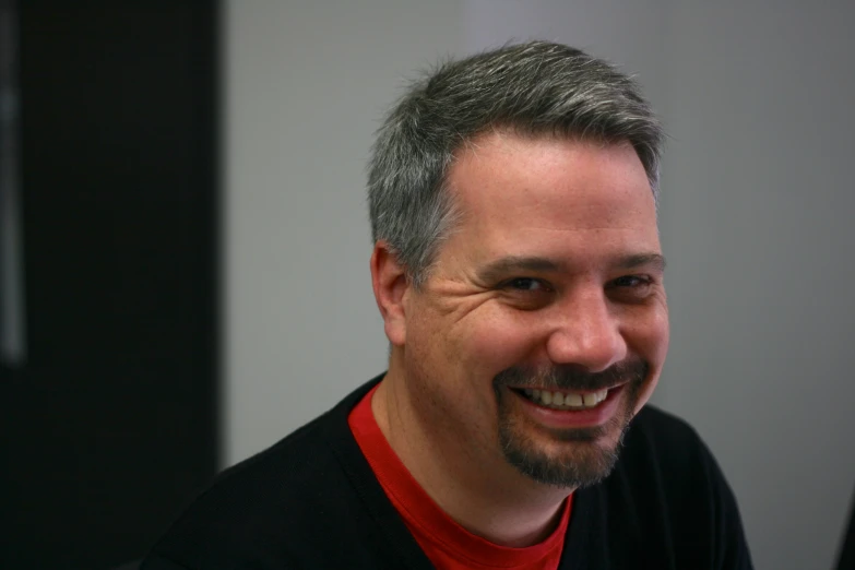 the man is smiling brightly wearing a red shirt