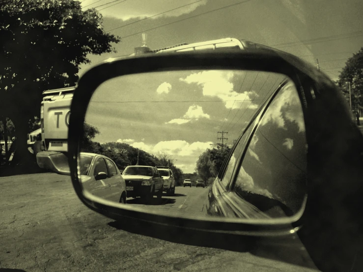 view in the side mirror of a car as the reflection of trees are seen in it