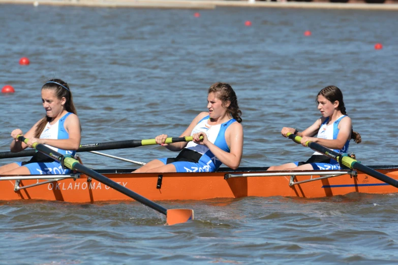 three girls rowing in the water on their own oars