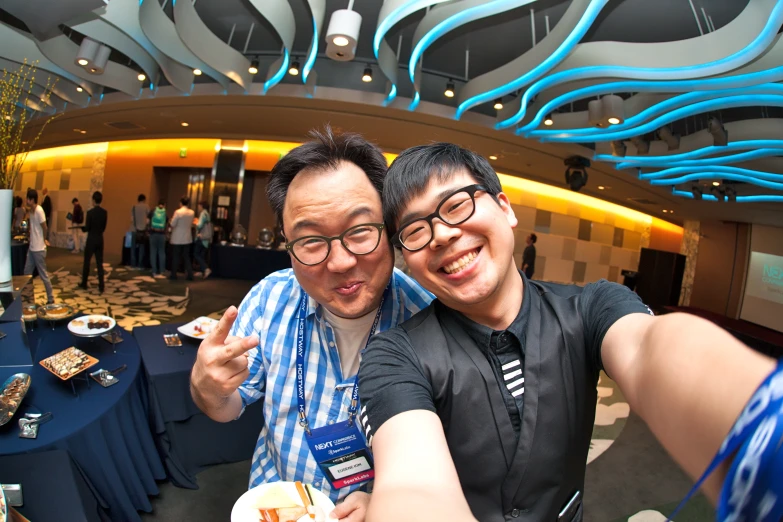 two men taking a selfie in front of a blue decorated ceiling