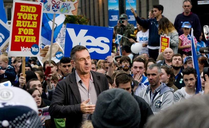 people standing with political signs, one holding a cell phone