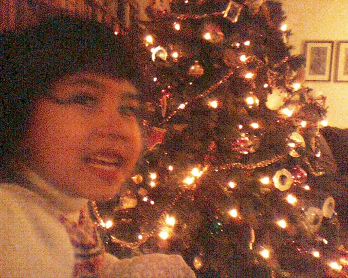 a girl is standing next to a lit christmas tree