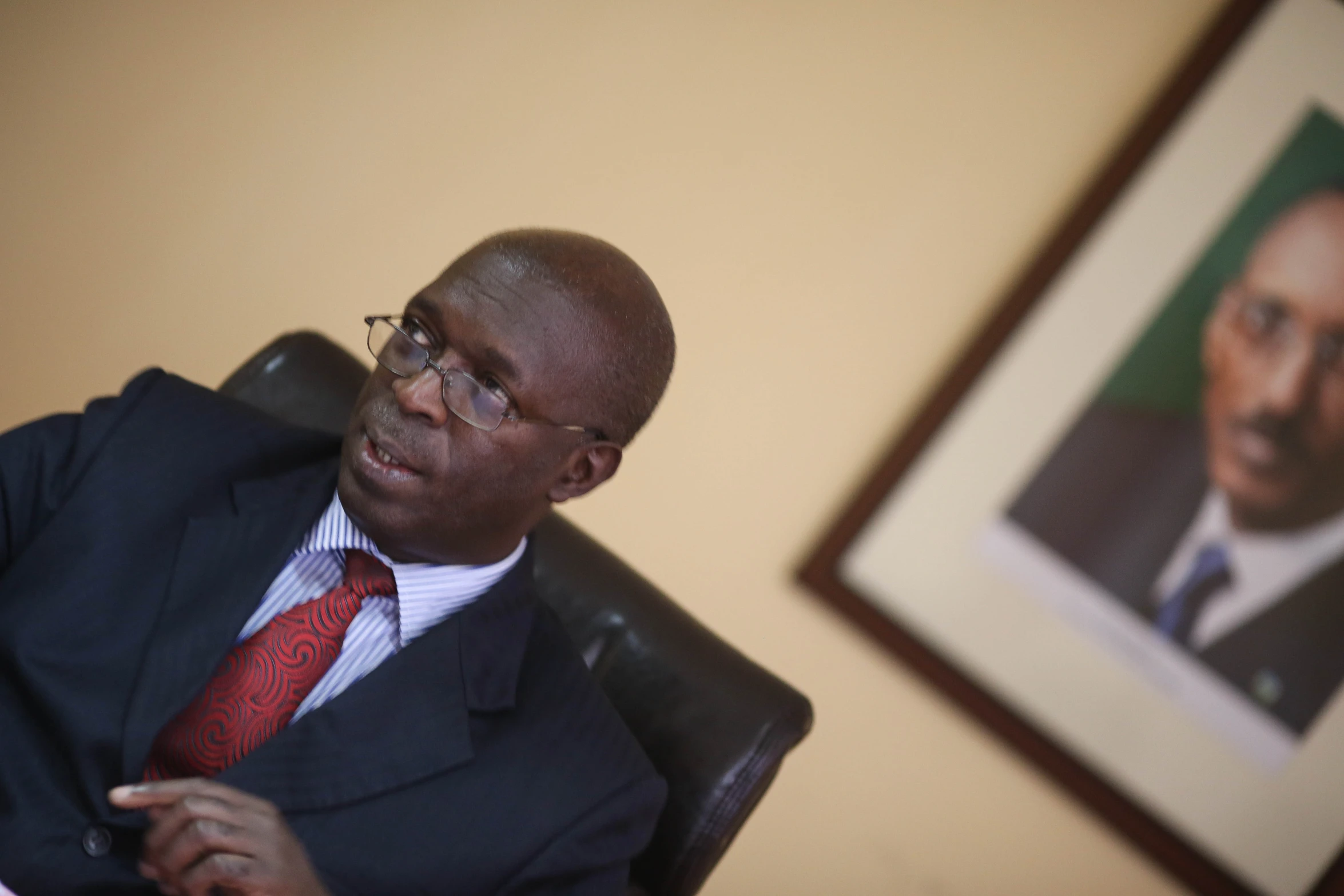 an african american man wearing a suit and red tie sitting in a chair