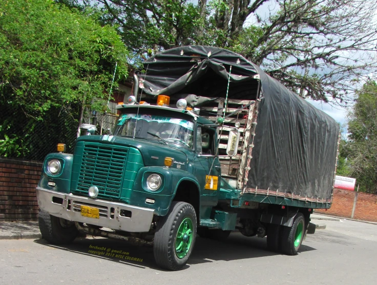 a green truck with its bed up is stopped in the street